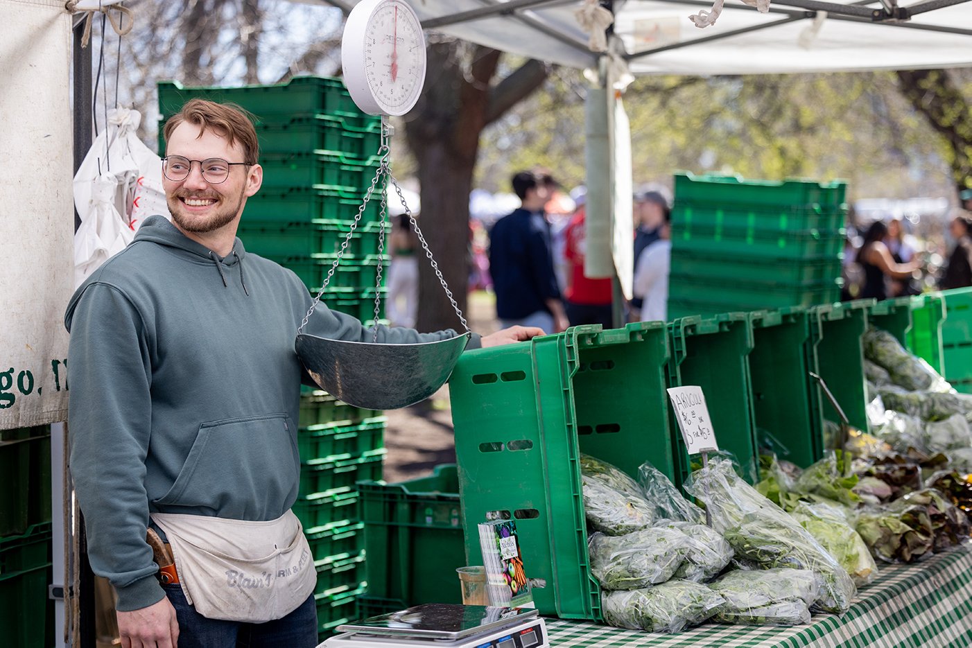 A man smiles while standing next to bags of greens on a table