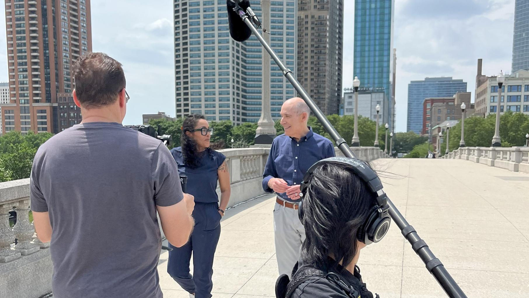 Geoffrey Baer interviews Eve Ewing for his spring 2026 program, Riding the Rails, while a camera operator and boom mic operator walk backwards.